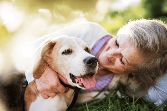 Older woman smiling and cuddling a happy dog on the grass outdoors.